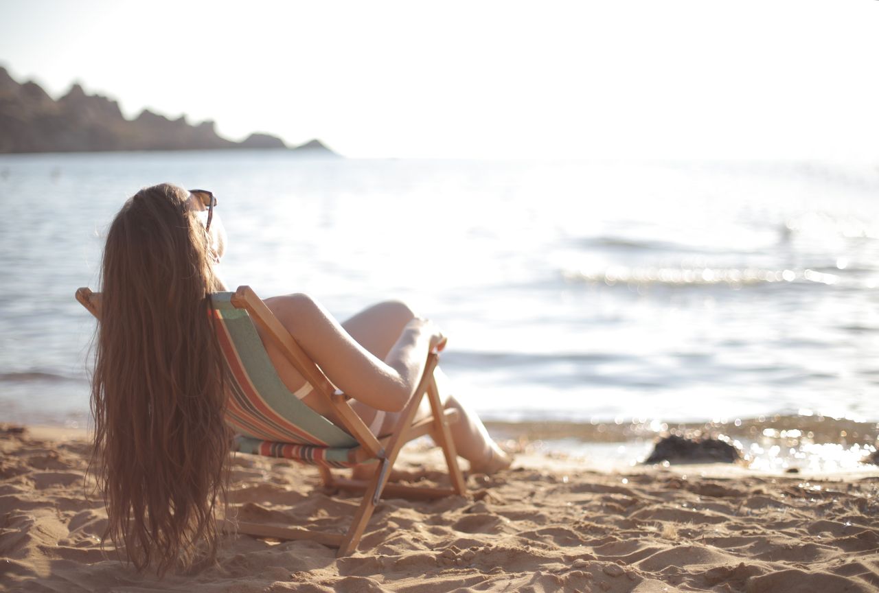 A woman sunbathes on a sandy beach in summer, enjoying relaxation by the ocean.
